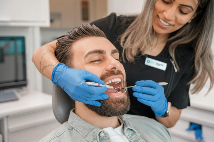 A dentist in blue gloves examining a man's teeth in a dental office